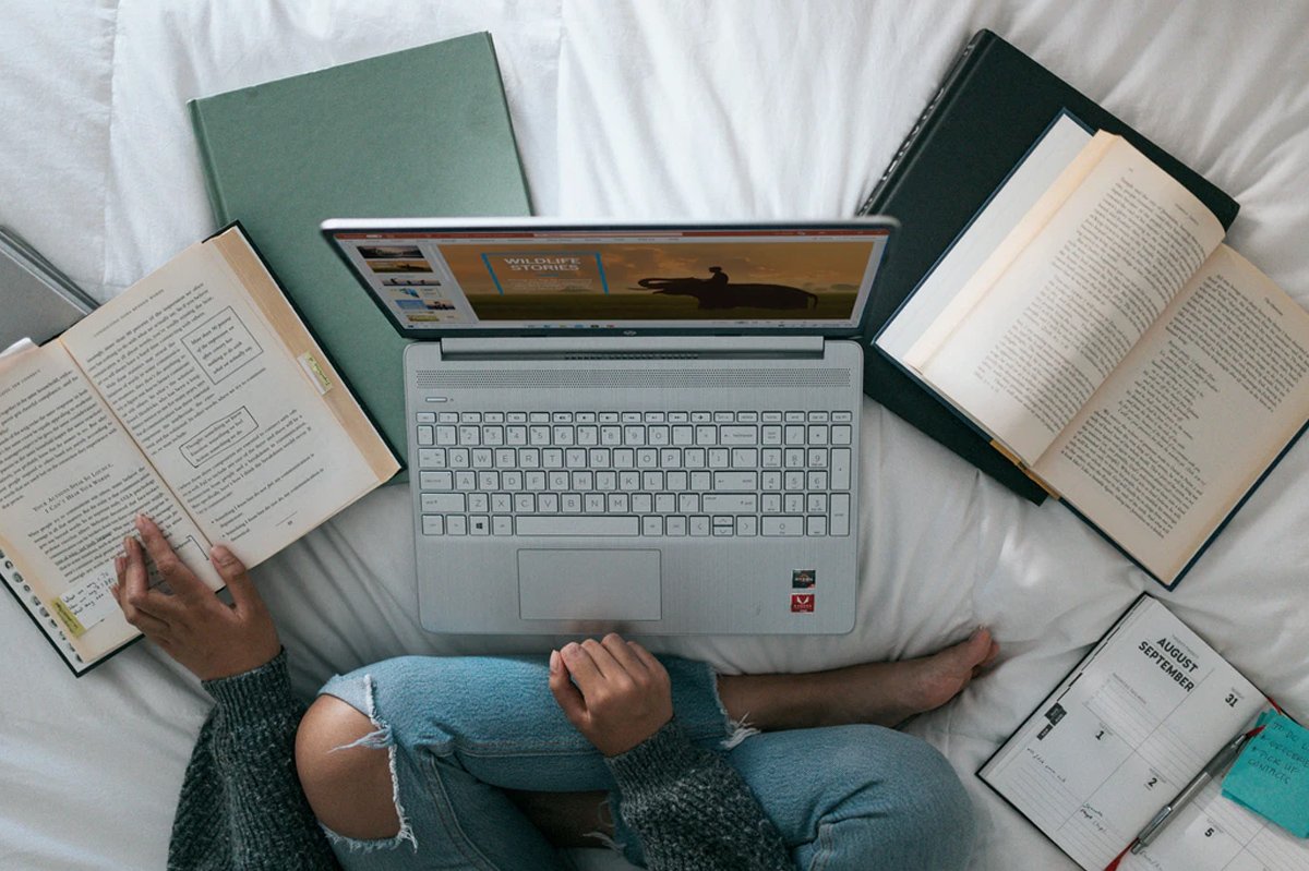 Portatil sobre cama con libros alrededor